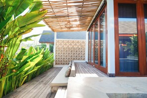 Un espacio de estar techado al aire libre con una terraza de madera, un banco acolchado y una pared con diseño geométrico.