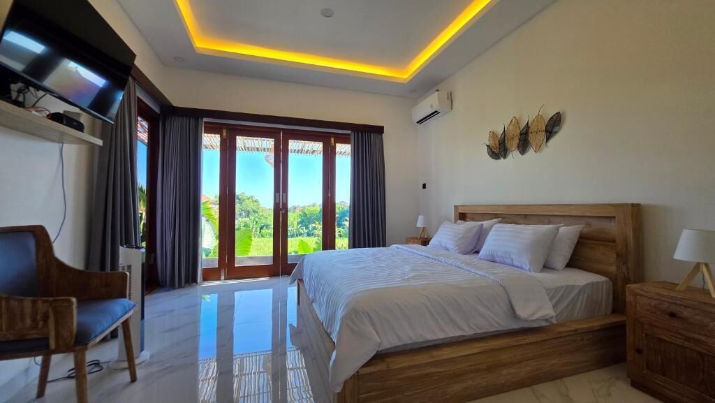 A bedroom with a bed, a TV, a desk, and a view of greenery outside.