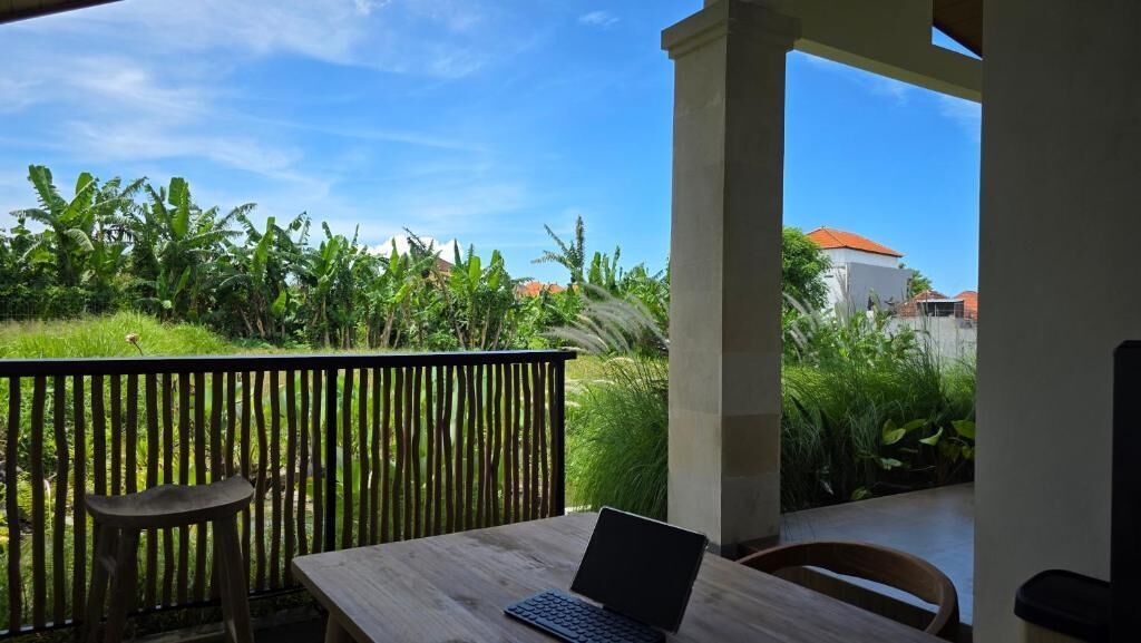 An outdoor seating area with a table and chairs, a laptop, and a view of a garden and buildings.