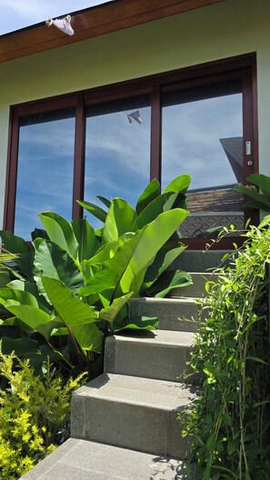 A building with a large glass window, a set of stone steps, and lush green plants.