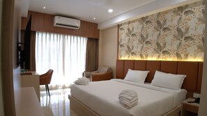 A hotel room with a bed, a desk, a chair, an air conditioning unit, and a decorative wall panel.