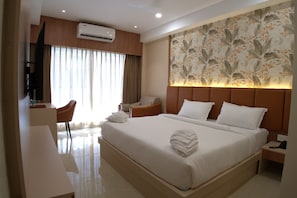 A hotel room with a bed, a desk, a chair, an air conditioning unit, and a decorative wall panel. - JRV RESIDENCE (Ambasamudram)