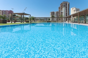 Ein Schwimmbecken mit Fliesenboden, umgeben von Bänken und einer Pergola.