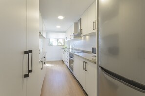 A modern kitchen with white cabinets, stainless steel appliances, and a wooden floor. - VACACIONES FRENTE AL MAR - Only families (Playa de Gandía)