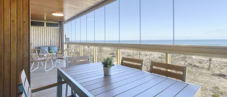 A wooden deck with a table and chairs, overlooking a beach.