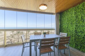 Ein Holztisch mit Stühlen in einem Raum, der ein großes Fenster mit Blick auf einen Strand hat.