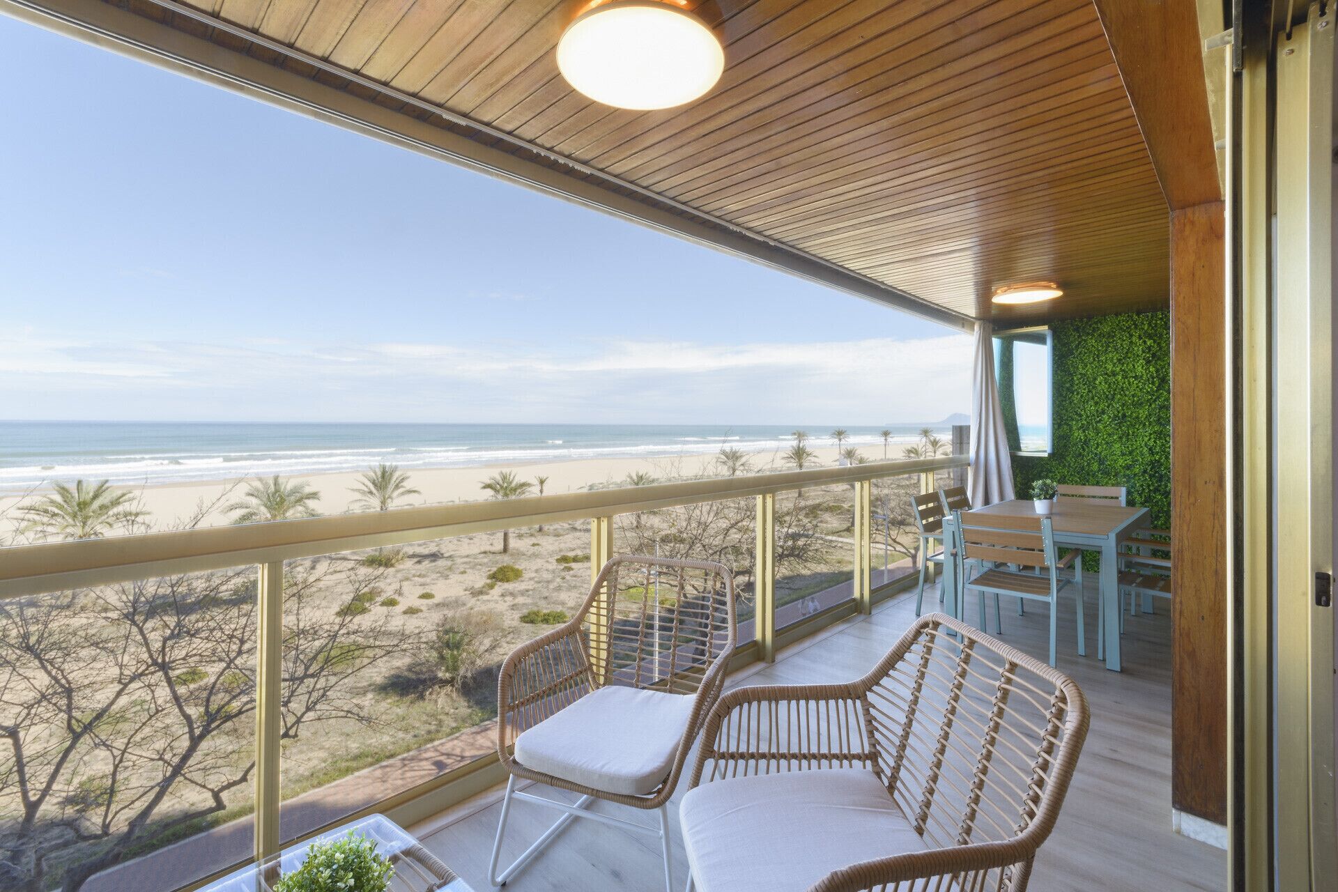 A balcony with wicker chairs, a table, and a view of the beach and ocean.