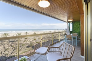 Ein Balkon mit Korbstühlen, einem Tisch und Blick auf den Strand und den Ozean.