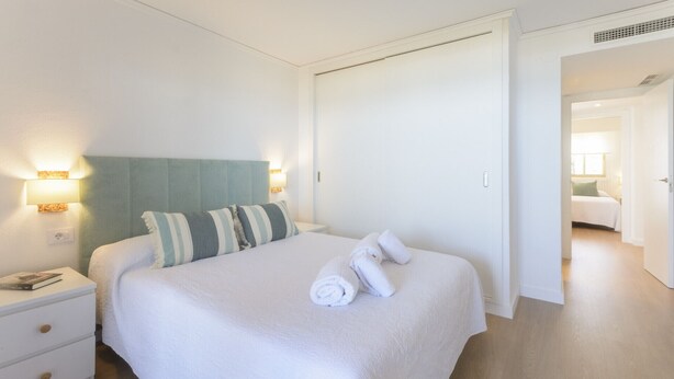 A hotel room with a bed, bedside tables, a nightstand, and a door leading to another room. - VACACIONES FRENTE AL MAR - Only families (Playa de Gandía)