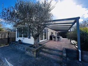 A covered patio area with a barbecue grill, outdoor seating, and a tree. - Beachfront Retreat With Private Canopy (Kamperland)