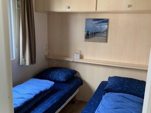 A small room with two beds, a shelf with a painting, and a window with curtains. - Beachfront Retreat With Private Canopy (Kamperland)