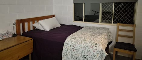 A bedroom with a bed, a window with a view, a wooden chair, and a bedside table.