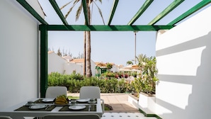 A dining area with a table set for two, surrounded by white walls and a green trellis. - Vivelorural Campo de Golf 76 (San Bartolomé de Tirajana)