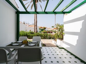 A dining area with a table set for two, surrounded by white walls and a green trellis. - Vivelorural Campo de Golf 76 (San Bartolomé de Tirajana)