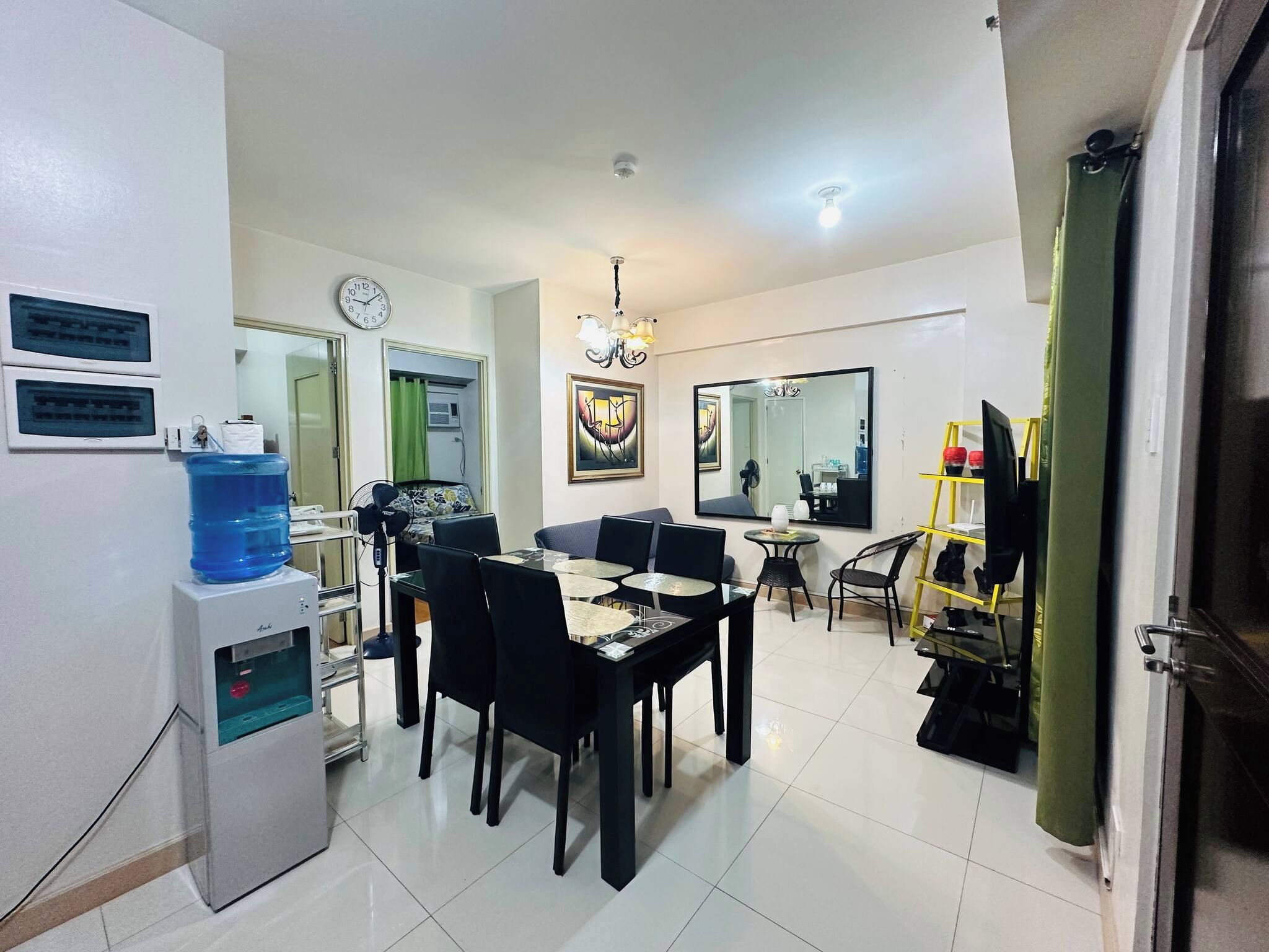 Un salon moderne comprenant un coin repas, un distributeur d’eau, une horloge et un grand miroir.
