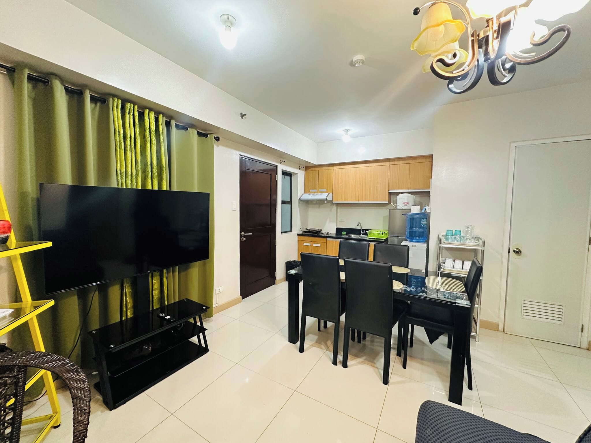 Una sala de estar con una televisión de pantalla plana, una mesa de comedor con sillas, una cocina con armarios y una puerta.