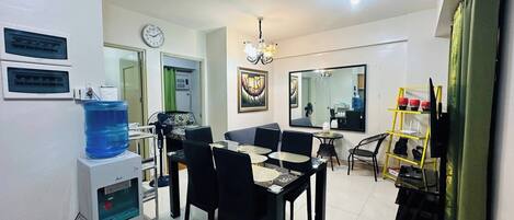 A modern living room with a dining area, a water dispenser, a clock, and a mirror.