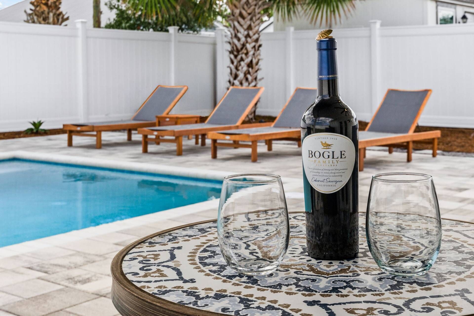 Ein Poolbereich mit einer Flasche Bogle Family Cabernet Sauvignon, zwei Gläsern und Liegestühlen.