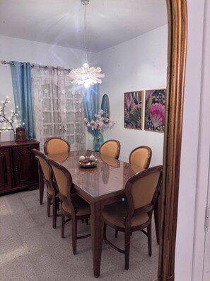 A dining room with a wooden table, six chairs, a vase with flowers, and two wall-mounted paintings. - The House of Olive Trees (La Marsa)
