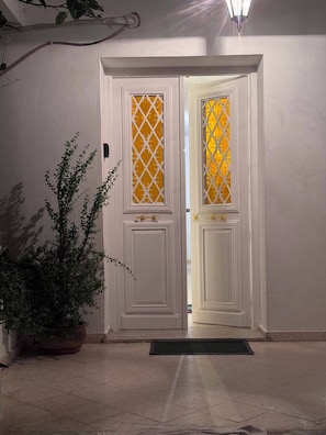 Uma porta branca com um painel de vidro decorativo e um vaso de planta ao lado.
