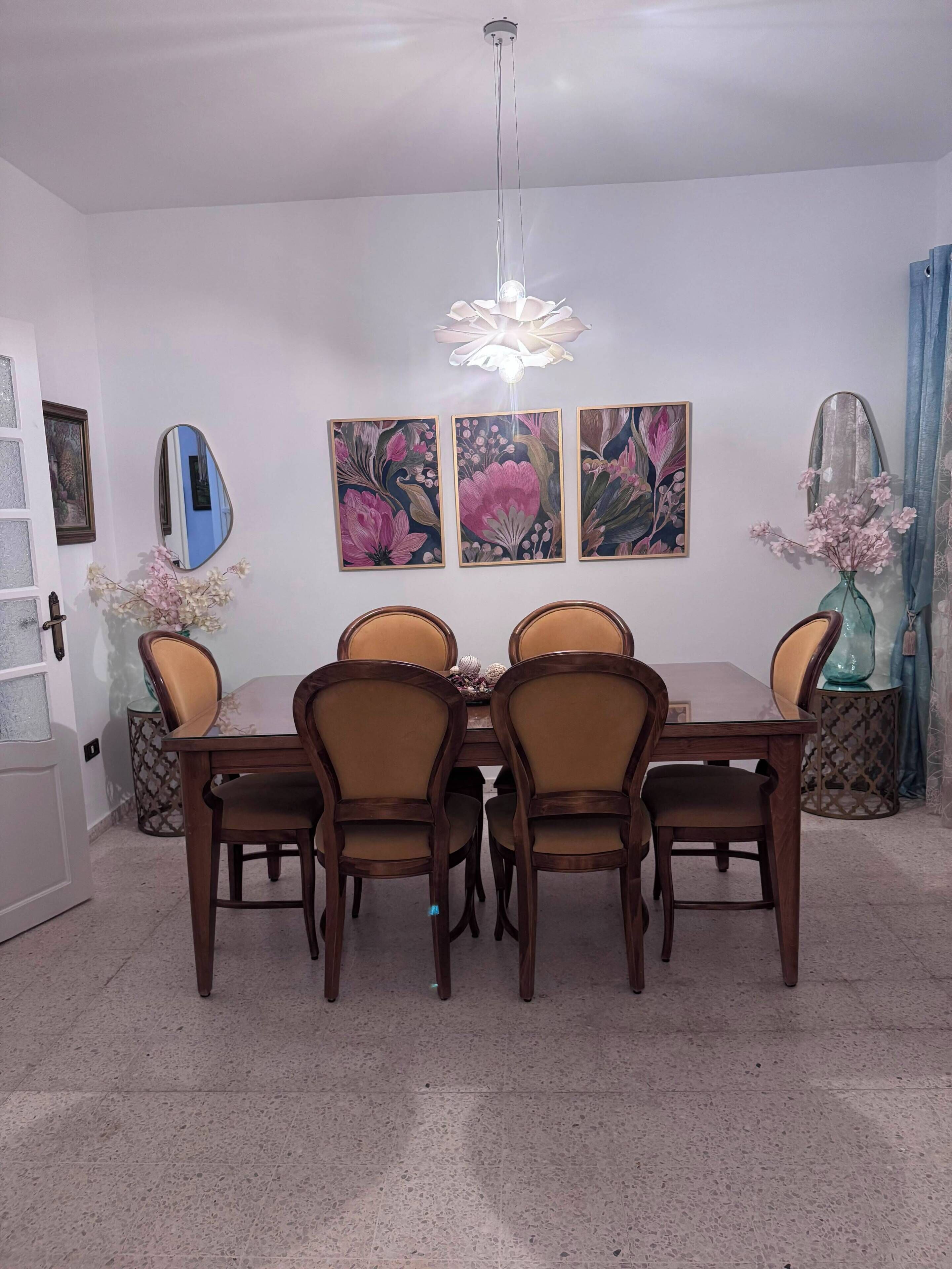 Un coin repas avec une table et des chaises en bois, un luminaire suspendu et des décorations murales à motifs floraux.