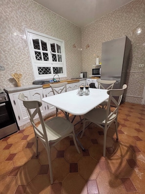 Uma cozinha compacta com mesa, cadeiras, geladeira, micro-ondas e máquina de lavar.