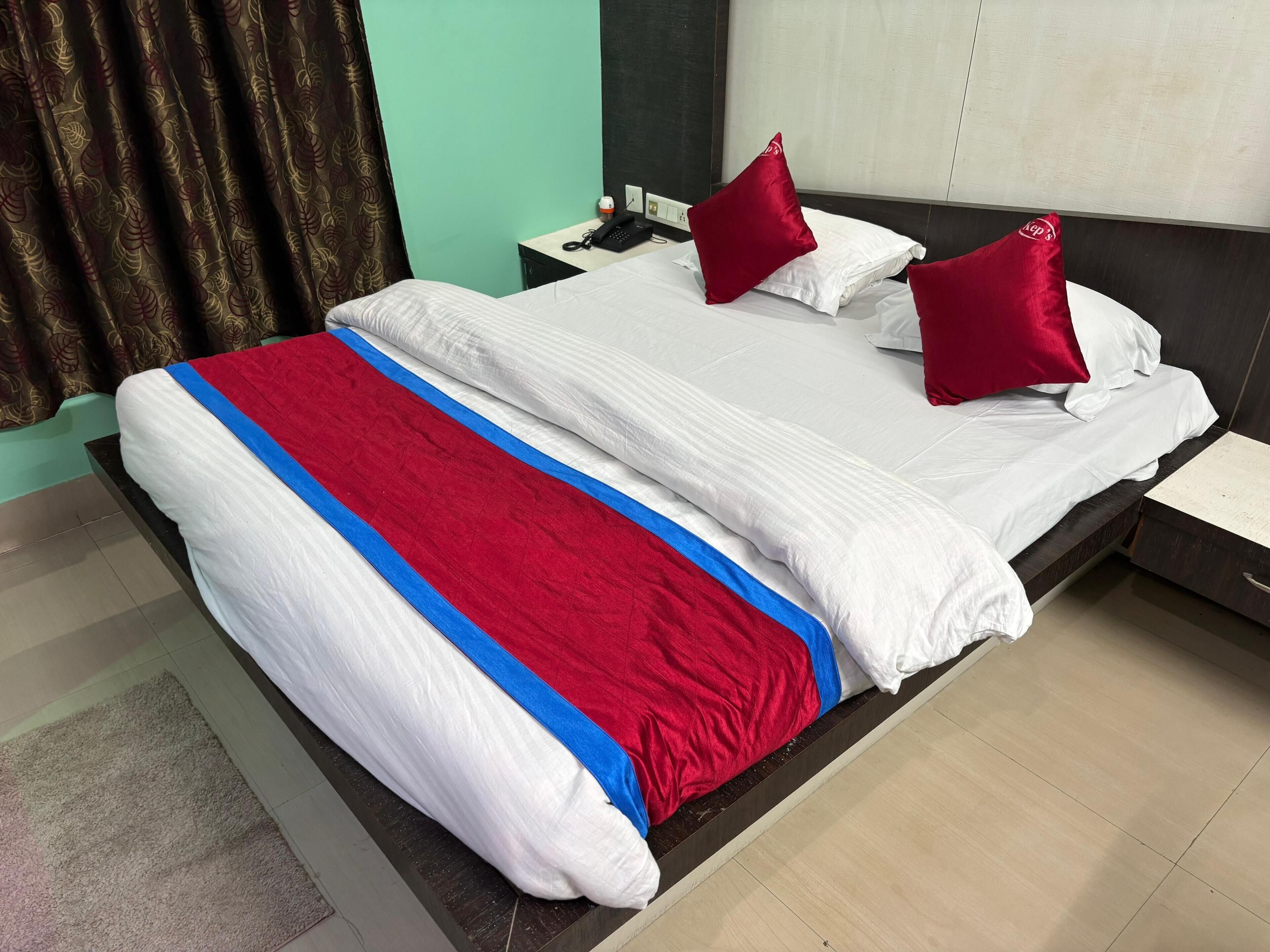 Una habitación de hotel con una cama, dos almohadas rojas, una mesita de noche con un teléfono y una mesita auxiliar.