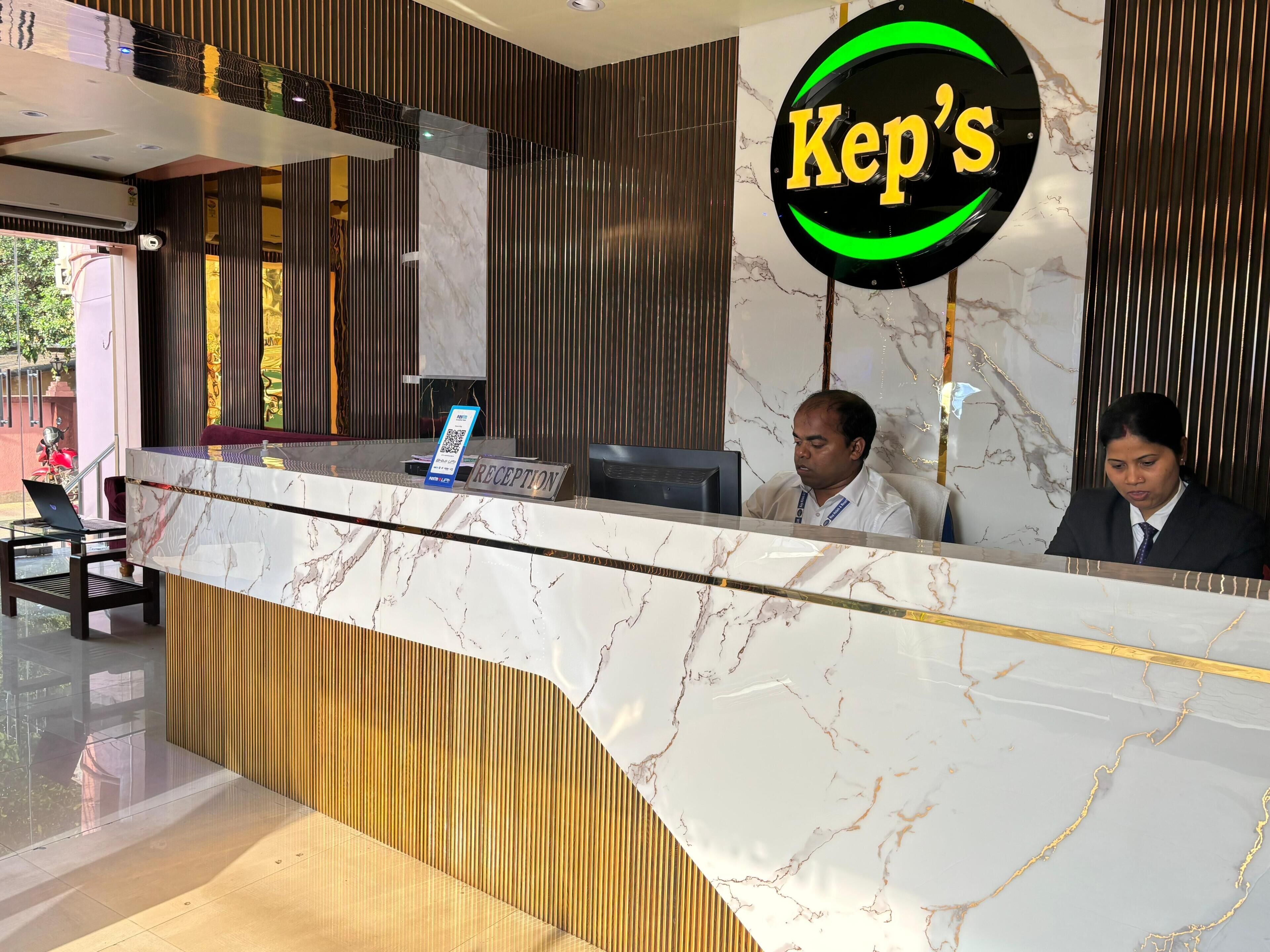 A reception desk with a marble countertop, a 'Kep's' sign, and two individuals seated behind it.