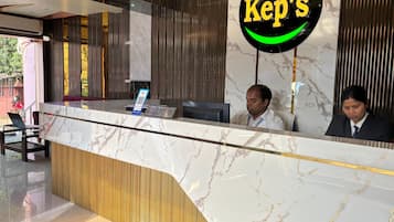 Un comptoir d’accueil avec un dessus en marbre, une enseigne « Kep’s » et deux personnes assises derrière.