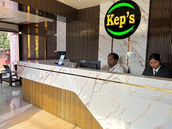 A reception desk with a marble countertop, a 'Kep's' sign, and two individuals seated behind it.