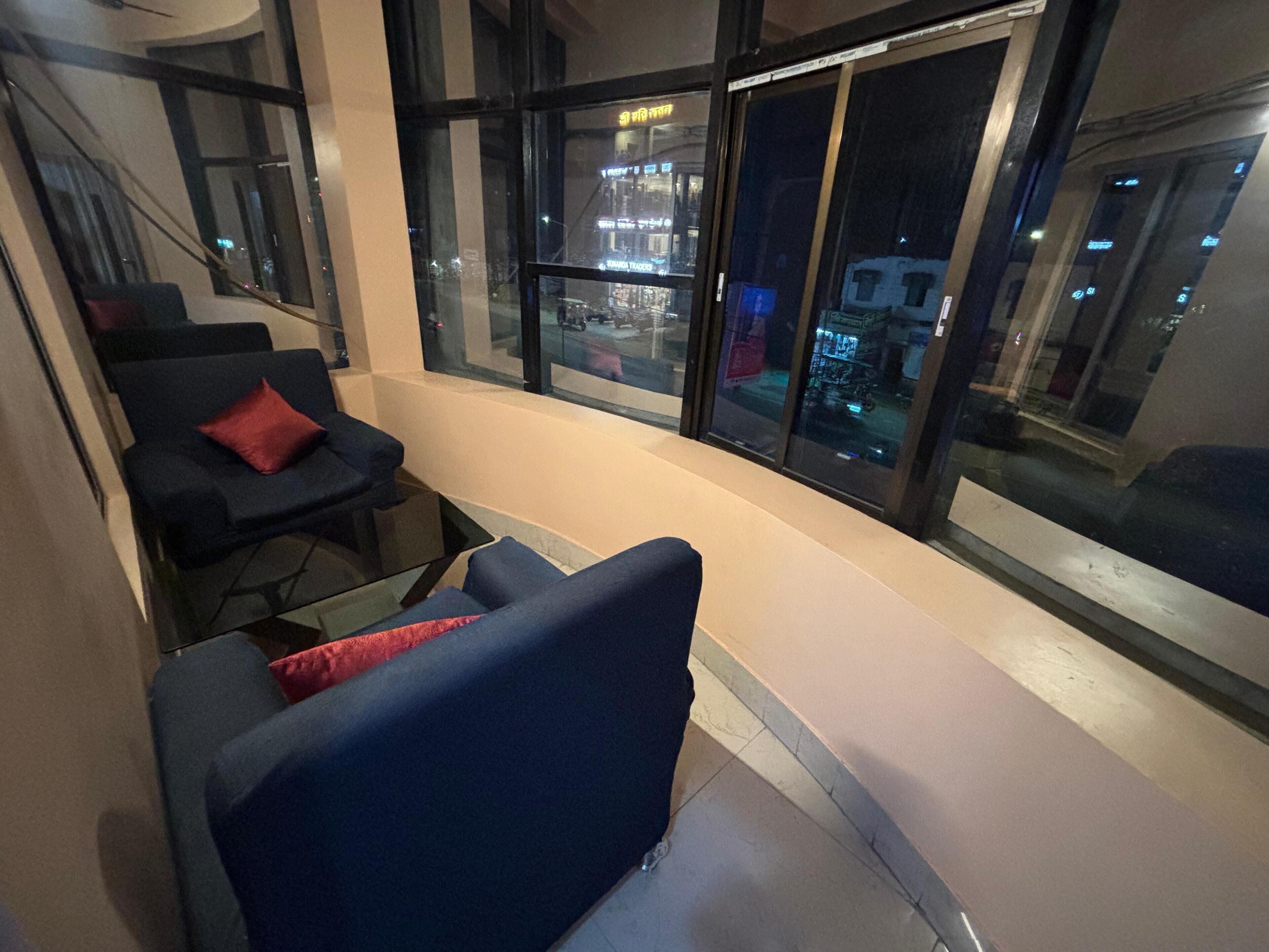 Habitación de hotel con zona de estar junto a la ventana, cama y vistas a la ciudad.