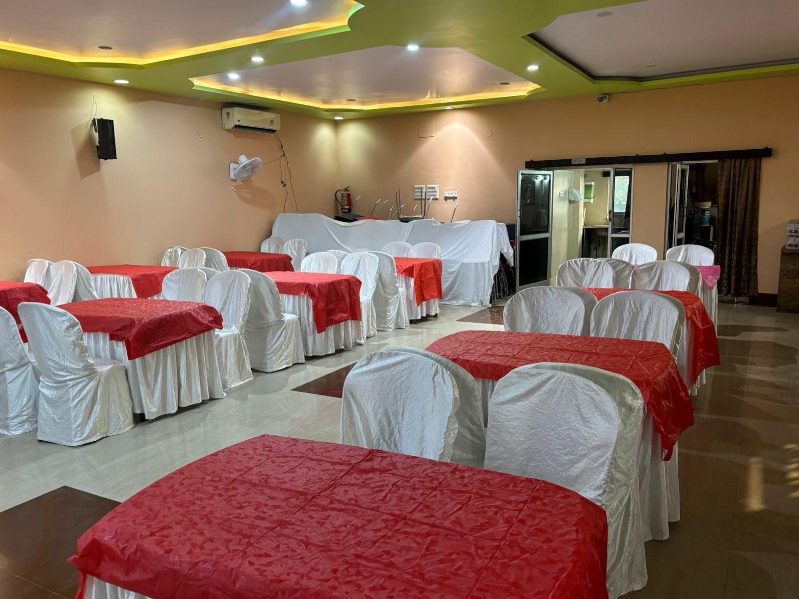 A banquet hall with tables covered in white and red tablecloths, arranged in rows.