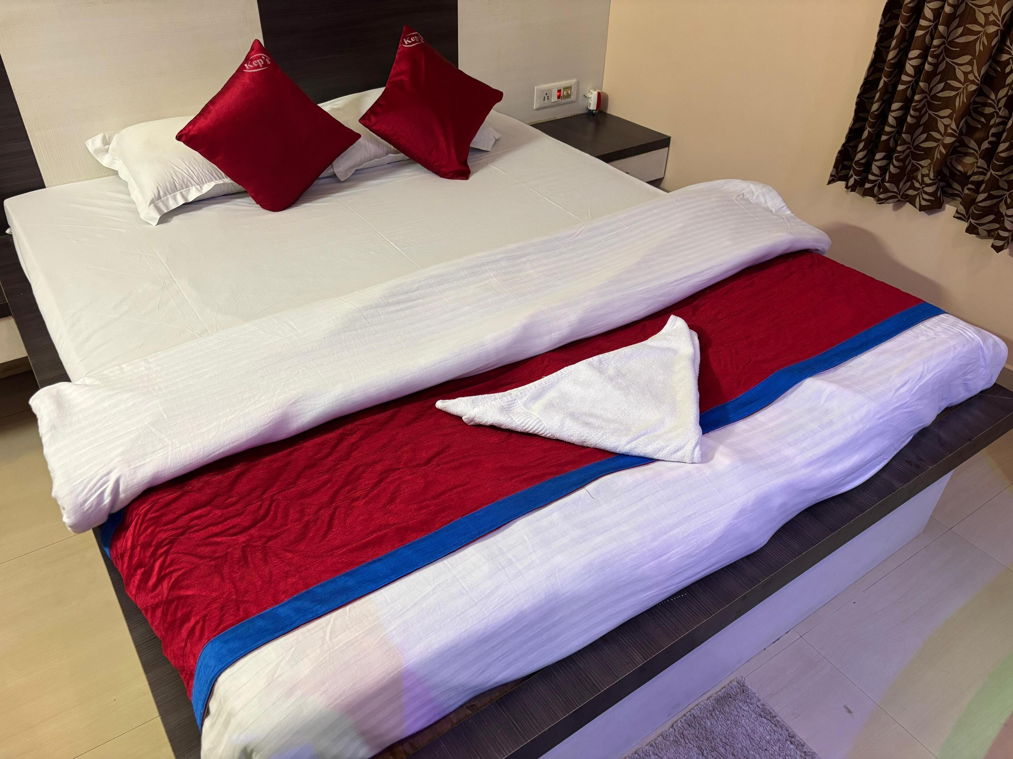 A neatly made bed with white and red bedding, a blue accent, and a pillow with a logo.