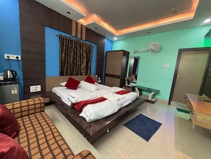 A hotel room with a large bed, a desk, a wardrobe, a mirror, and a fan.