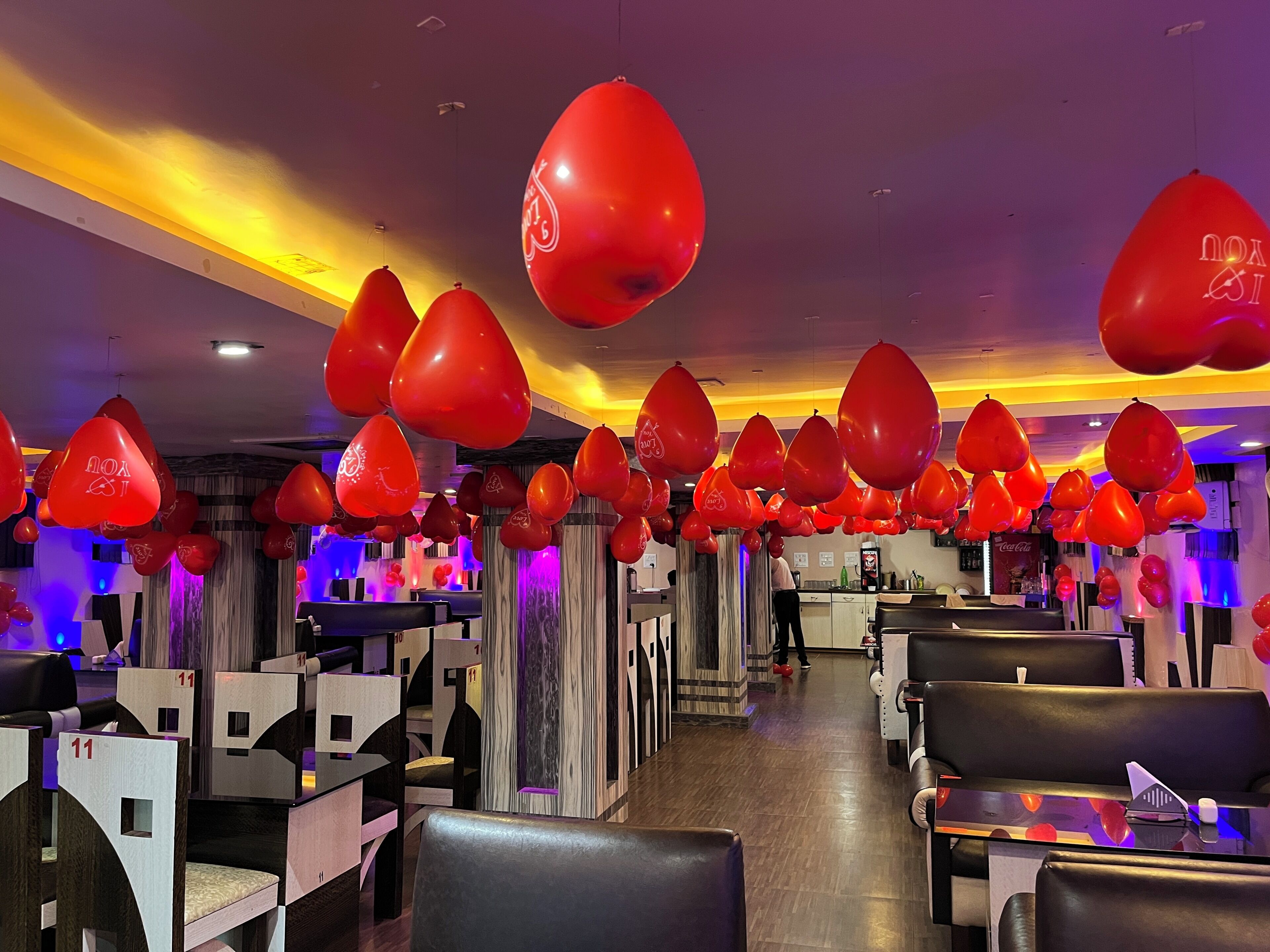 A restaurant interior with booths and tables, red balloons, and a bar area.
