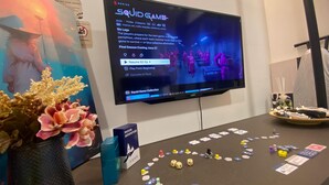 Un televisor mostrando una interfaz de juego, una mesa con piezas de juego y un jarrón decorativo.