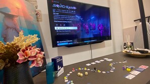 Ein Fernseher zeigt eine Spieloberfläche, ein Tisch mit Spielsteinen und eine dekorative Vase.