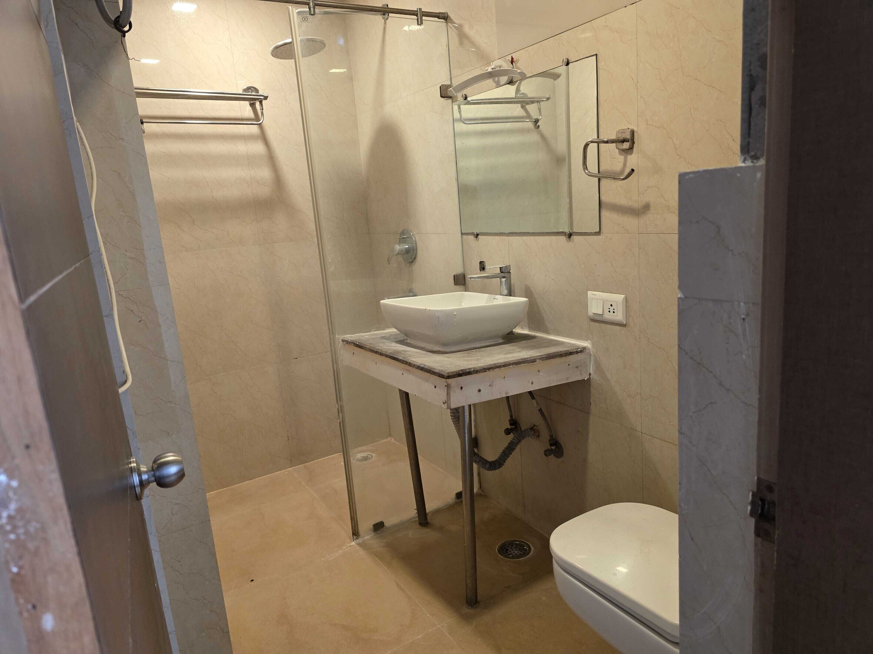 A bathroom with a glass shower enclosure, a white sink, a mirror, and a toilet.