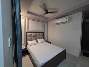 A bedroom with a bed, a ceiling fan, an air conditioning unit, and a nightstand.