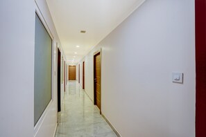 A corridor with doors on both sides, a tiled floor, and a ceiling with recessed lighting. - Super Deluxe Room Mauji's (Prayagraj)