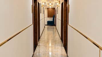 A hotel hallway with marble flooring, wall sconces, and a blue chair.