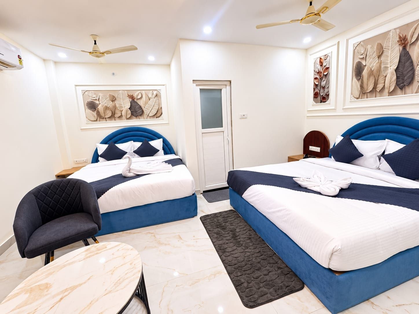 Une chambre d’hôtel avec deux lits, une chaise, une table, des ventilateurs de plafond et des œuvres d’art accrochées aux murs.