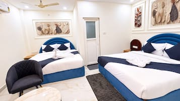 A hotel room with two beds, a chair, a table, ceiling fans, and artwork on the walls.