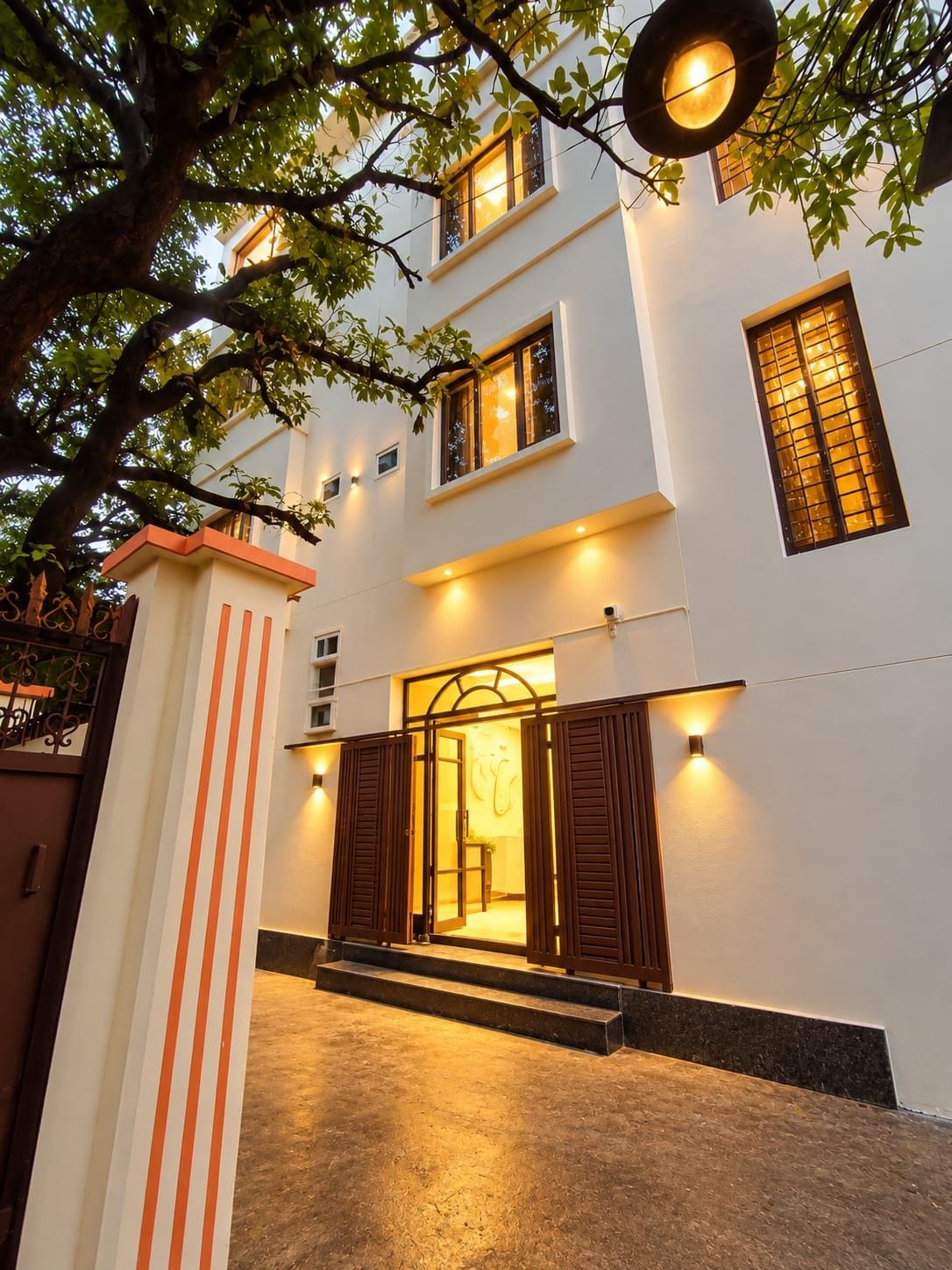 A two-story building with a well-lit entrance, a staircase leading to the door, and a tree in the foreground.
