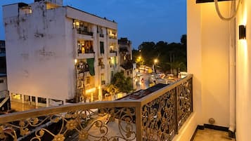 A balcony with a decorative railing, an air conditioning unit, and a view of a cityscape at dusk.