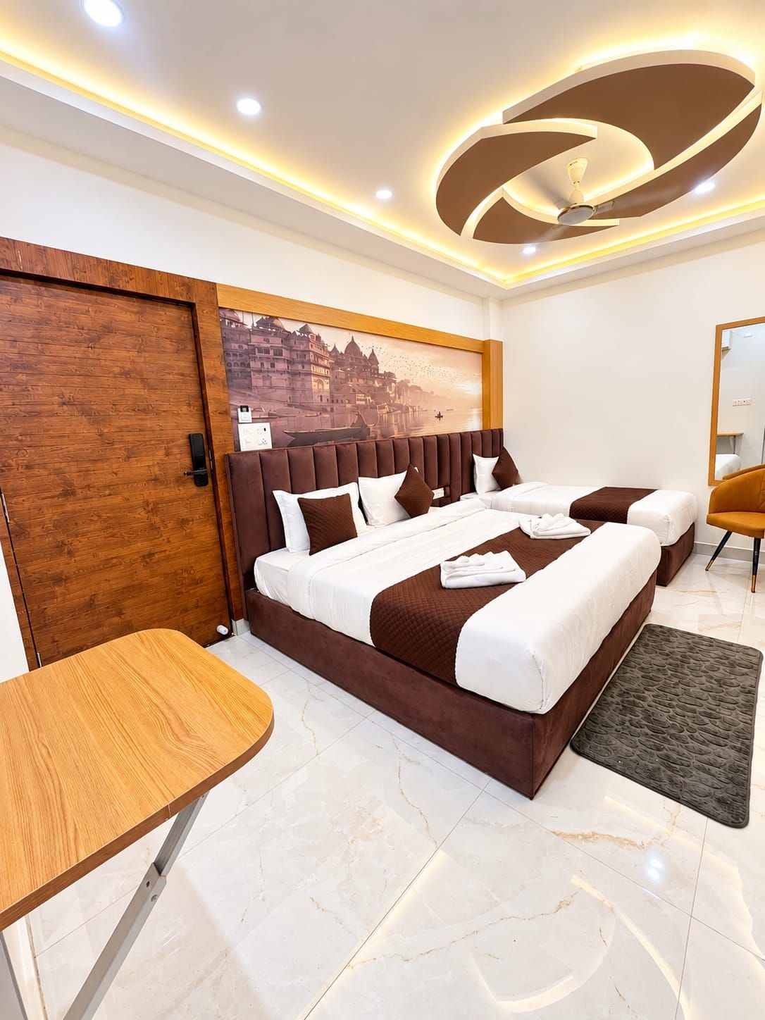 A modern hotel room with a large bed, a wooden door, a small table, and a view of a cityscape.