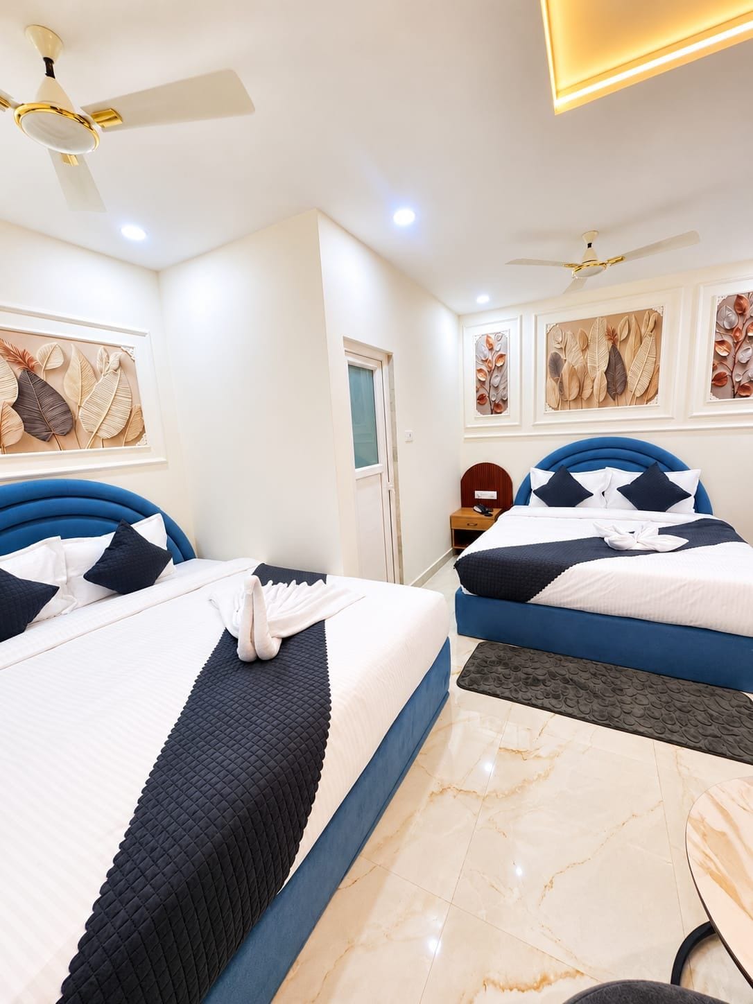 Habitación de hotel con dos camas, ventilador de techo, obras de arte en las paredes y suelo de mármol.