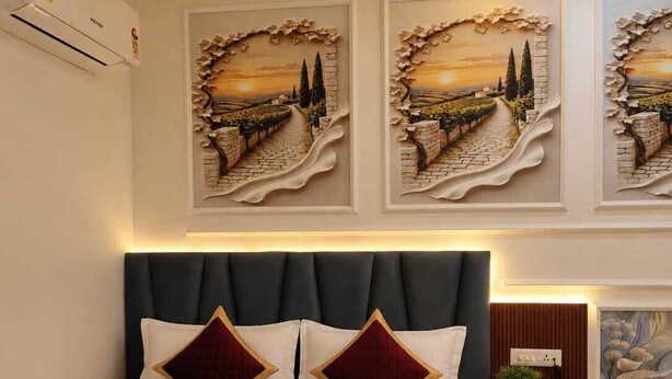 A hotel room with a bed, a nightstand, a wall-mounted air conditioner, and a ceiling fan. - Hotel Rajyashree Retreat (Varanasi)