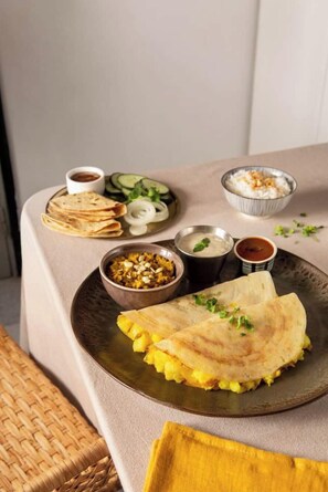 Una mesa con un plato de comida, que incluye un pan plano doblado, un tazón de curry y un plato con pepinos y cebollas en rodajas.