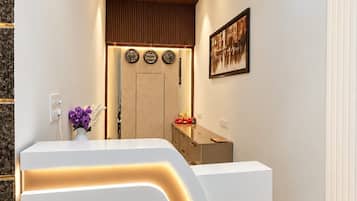 A reception area with a modern design, featuring a reception desk, a ceiling fan, wall-mounted clocks, and a framed picture.